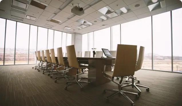 A large meeting room with a meeting table surrounded by office chairs, with panoramic windows in the background.