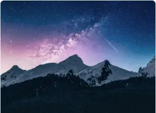 Starry night sky over majestic mountains with a visible shooting star.
