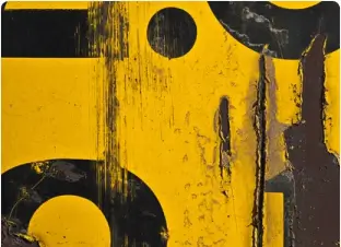 Yellow weathered surface with black markings and paint wear, creating an abstract pattern.