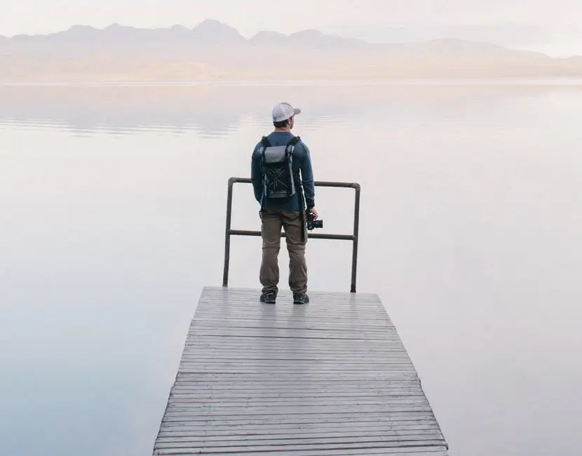 A man stands on a dock, gazing thoughtfully over a serene lake, surrounded by nature's tranquility.